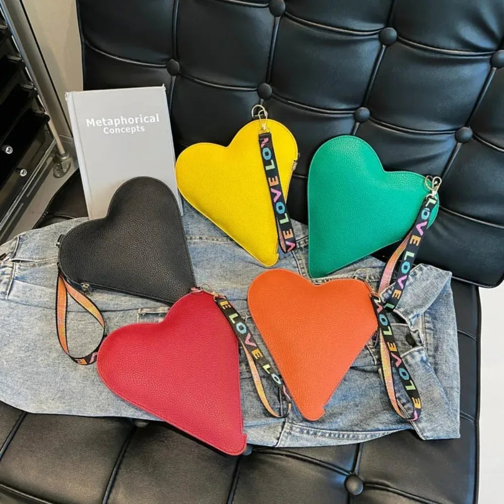 A collection of heart-shaped PU coin purses in yellow, green, and orange resting on a denim shirt next to a book.