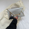 Silver crocodile pattern PU envelope clutch with gold accents held by a hand against a cream blazer.