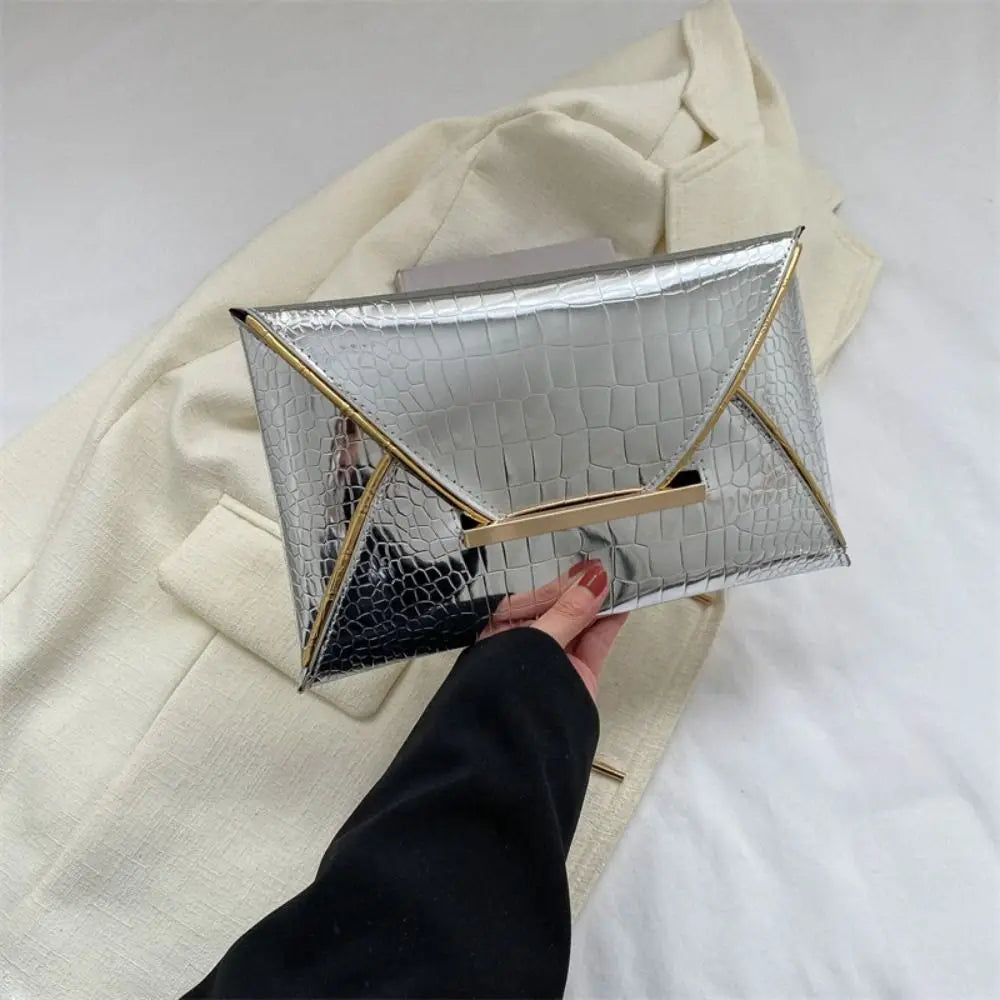 Silver crocodile pattern PU envelope clutch with gold accents held by a hand against a cream blazer.