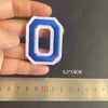 A hand holds a blue and white embroidered letter O patch, measuring 5.2 by 3.8 cm against a ruler.
