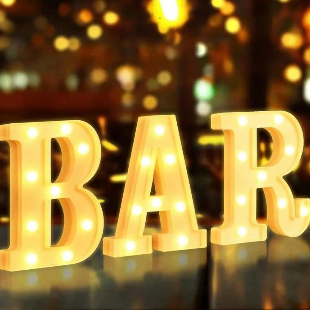 Wooden letters spelling BAR illuminated with warm white LED lights on a reflective surface.