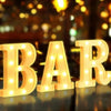 Golden LED letter sign spelling BAR with warm lights on a reflective surface.