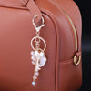 A gold-toned keychain charm featuring a rhinestone bow and heart attached to a leather handbag strap.