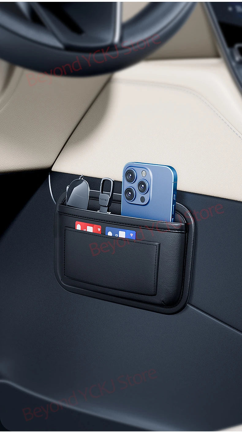 A blue smartphone is stored in a black car seat side pocket organizer with various accessories.