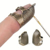 A vintage metal sewing thimble with a finger protector ring is shown being held by a hand.