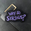 A purple embroidered patch with the text Why So Serious is attached to a black leather item.