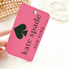 A pink card holder with a black spade design and the name Kate Spade New York is shown on a white surface.
