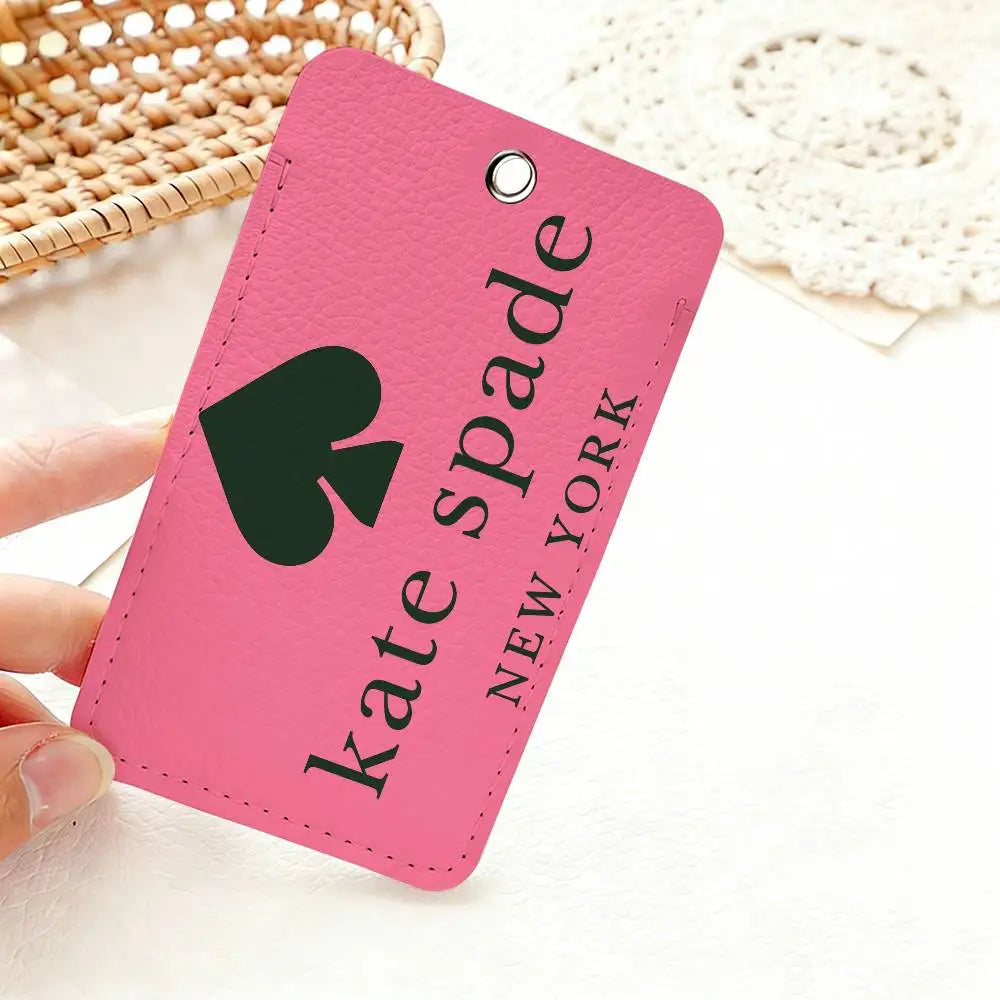 A pink card holder with a black spade design and the name Kate Spade New York is shown on a white surface.