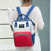 A white and blue insulated canvas mummy diaper bag with a hanging hook worn by a person.