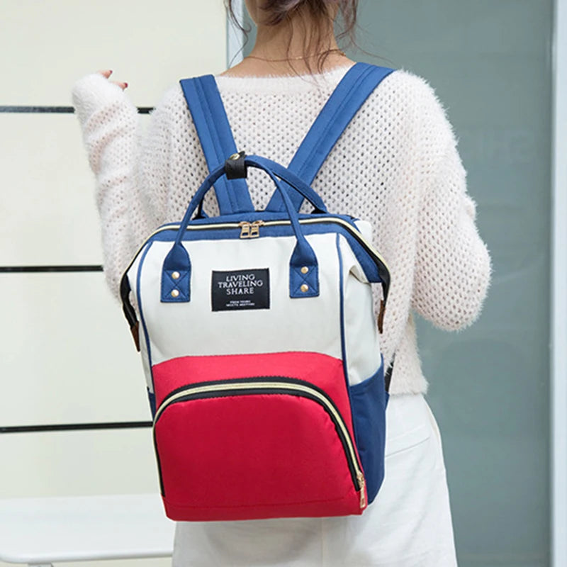 A white and blue insulated canvas mummy diaper bag with a hanging hook worn by a person.