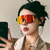 A woman wearing orange-tinted cycling sunglasses against a light background.