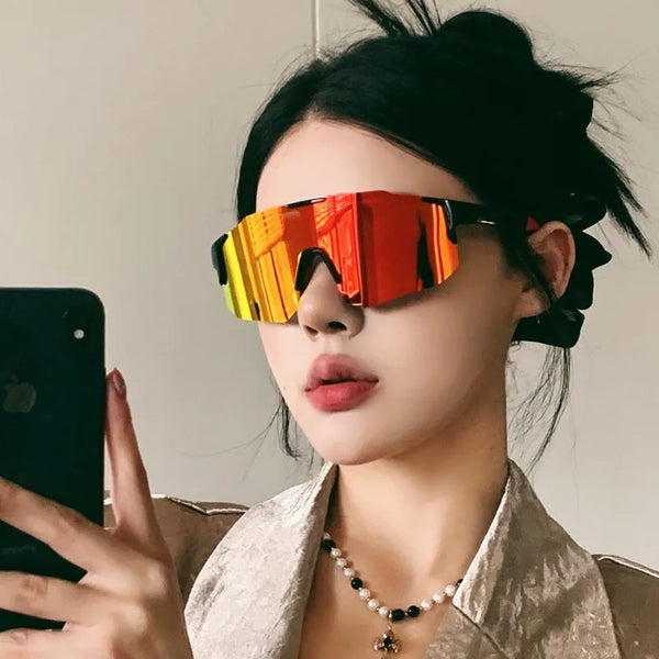 A woman wearing orange-tinted cycling sunglasses against a light background.