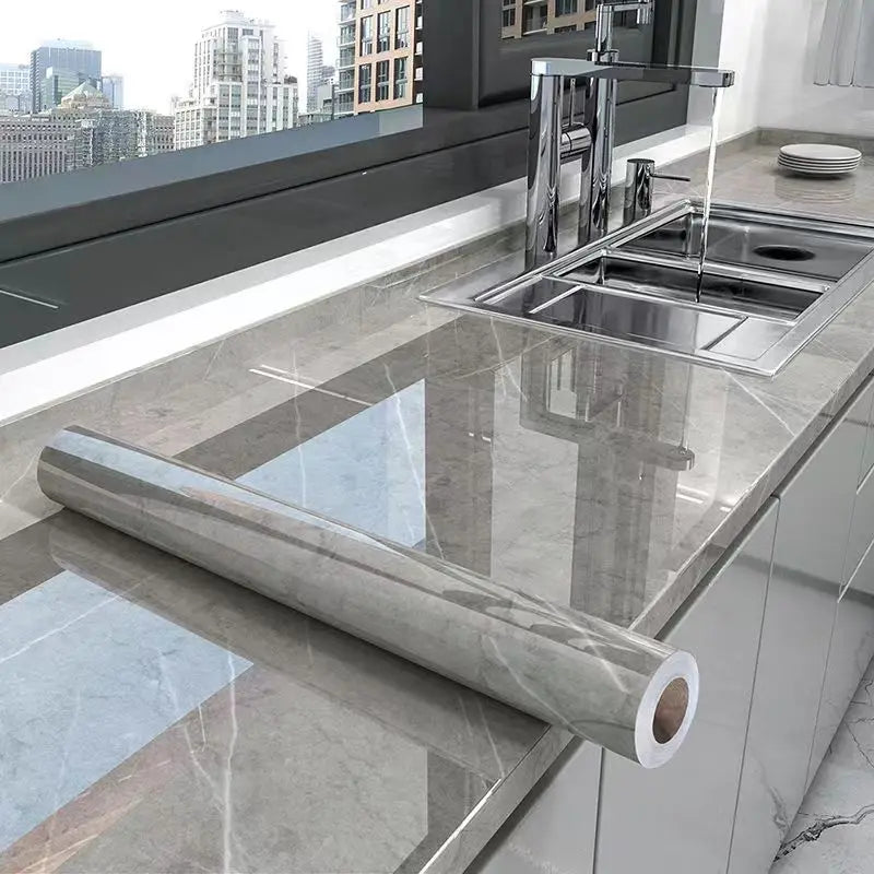 A stainless steel kitchen sink and faucet installed in a marble countertop, with a rolled marble effect film lying on the sur