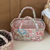 A pink quilted fabric storage basket with a handle and floral pattern sits next to another similar basket.