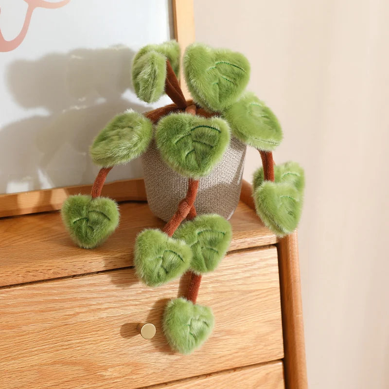 A small potted plant made of soft green faux leaves resembling a pothos, sitting on a wooden surface.
