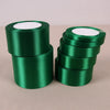 A stack of dark green lustrous satin ribbon rolls for gift wrapping and crafts.