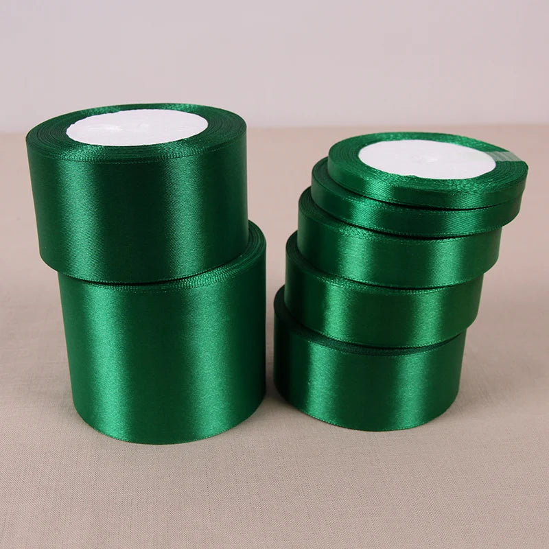 A stack of dark green lustrous satin ribbon rolls for gift wrapping and crafts.