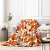 An orange and yellow maple leaf patterned flannel throw blanket draped over a gray sofa.