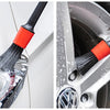 A close-up of a black scrubbing brush with an orange handle cleaning a car wheel rim.