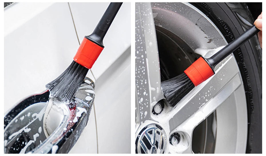 A close-up of a black scrubbing brush with an orange handle cleaning a car wheel rim.