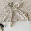 A white pearl bow keychain with a heart charm and delicate lace details