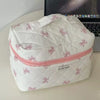 A white cosmetic bag with pink bow print and multi-compartment organization resting on a white surface.
