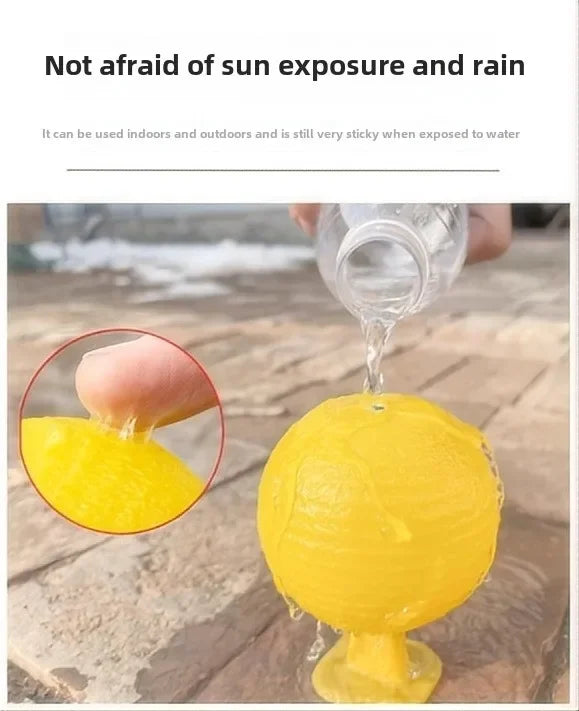 A yellow sticky fruit fly trap ball is dripping liquid onto a glass, set outdoors on a wooden surface.