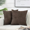 A set of two dark brown corduroy patchwork throw pillow covers with vertical stitching on a white sofa.