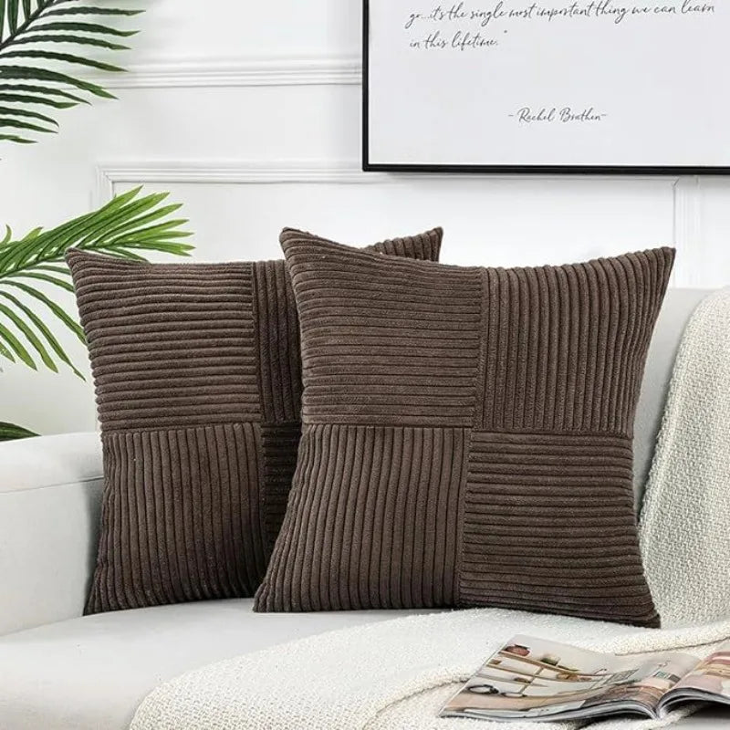 A set of two dark brown corduroy patchwork throw pillow covers with vertical stitching on a white sofa.