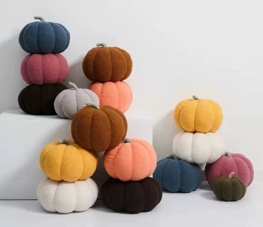 A stack of soft, round plush pillows shaped like pumpkins in various earthy and pastel colors.