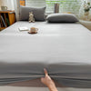 A close-up view of a solid gray fitted sheet on a bed, with a hand touching the fabric.