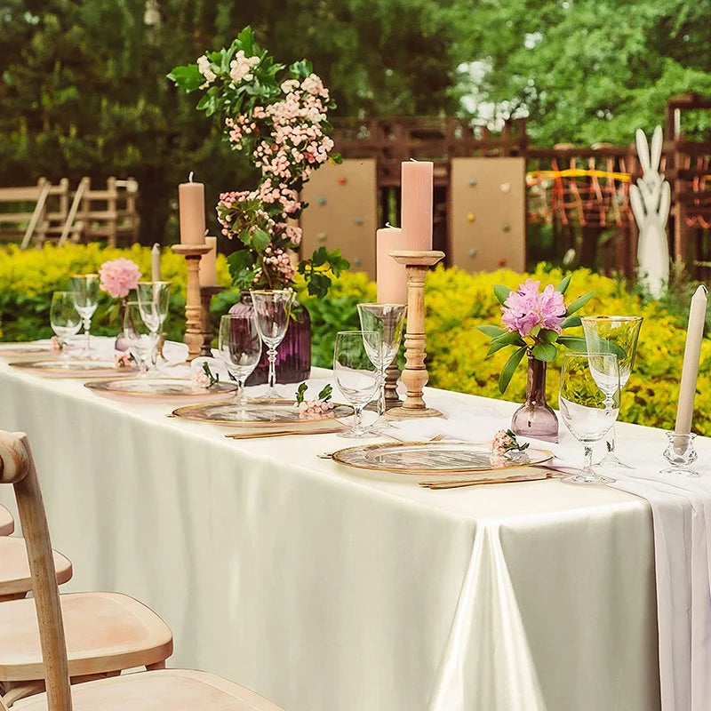 A long table set for a wedding or formal dinner with white satin tablecloths, candles, and floral arrangements.