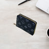 A black zippered card holder wallet with a gold zipper is placed on a light wooden surface next to a notebook and a laptop.