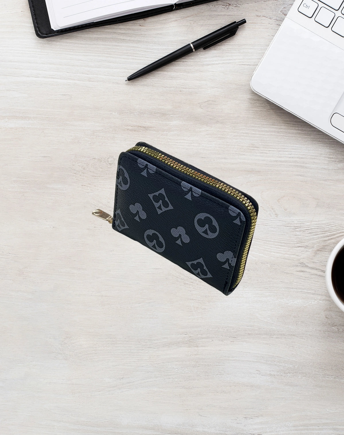 A black zippered card holder wallet with a gold zipper is placed on a light wooden surface next to a notebook and a laptop.