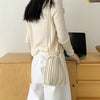 A woman wearing a cream sweater and white pants holds an elegant pleated faux leather crossbody bag.