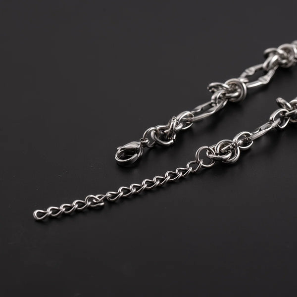 A silver titanium steel chain bracelet with knot details laid diagonally on a dark background.