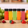 A row of six leak-proof clear plastic juice bottles filled with various fruit juices in bright colors on a wooden surface.