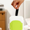 A hand is dispensing a black wipe from a white and lime green refillable wipe dispenser box.