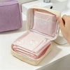 A light pink storage pouch with a lid is open, revealing stacked sanitary napkins and cosmetic items in a beige box.