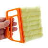 An orange dusting brush with a yellow fuzzy head is held by a hand.