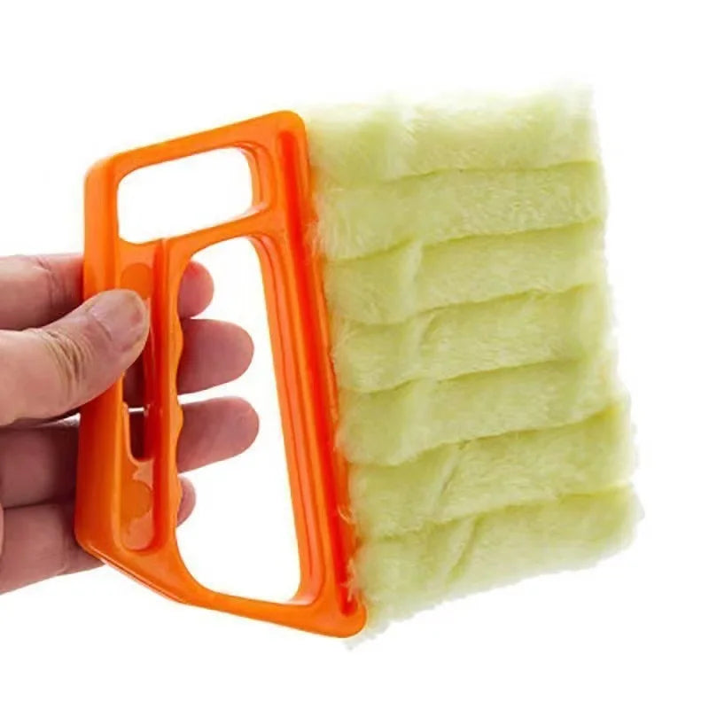 An orange dusting brush with a yellow fuzzy head is held by a hand.