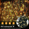 Close-up of warm yellow LED string lights strung through dark branches in an outdoor setting.