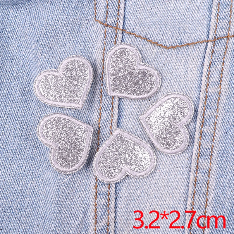 A set of five silver glitter heart iron-on embroidered patches placed on a light blue denim fabric.
