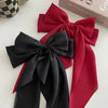 A black silk bow hair clip and ponytail holder with a red ribbon lying on a white surface.