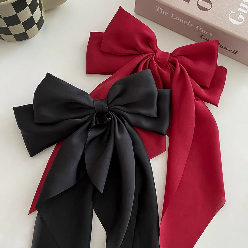 A black silk bow hair clip and ponytail holder with a red ribbon lying on a white surface.