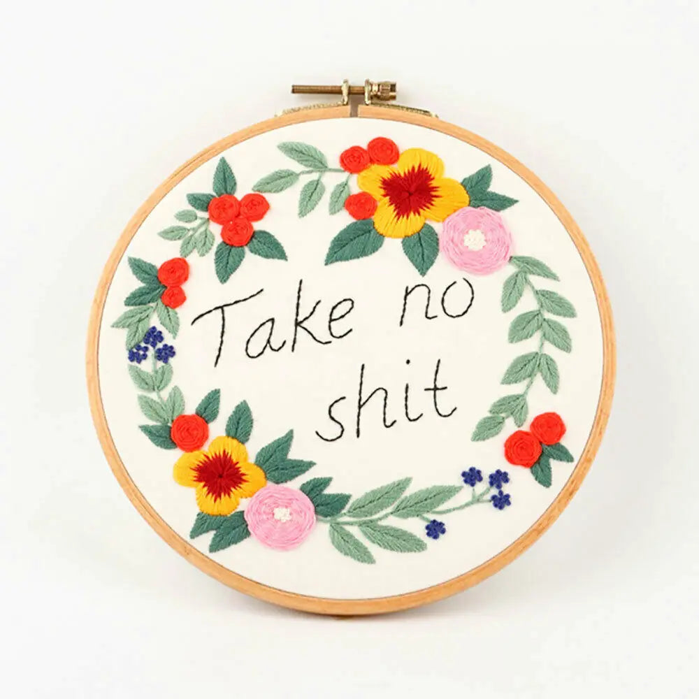 A circular embroidery hoop featuring a floral wreath of red, yellow, and pink flowers and green leaves with the text Take no 