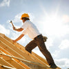 A construction worker wearing a yellow hard hat and white shirt is installing wooden planks on a slanted structure.