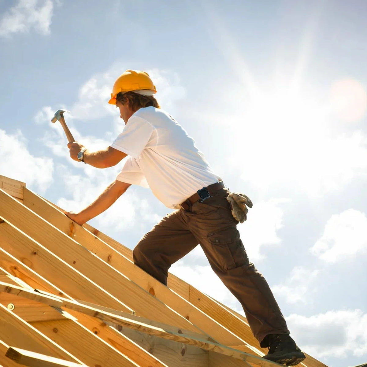 A construction worker wearing a yellow hard hat and white shirt is installing wooden planks on a slanted structure.