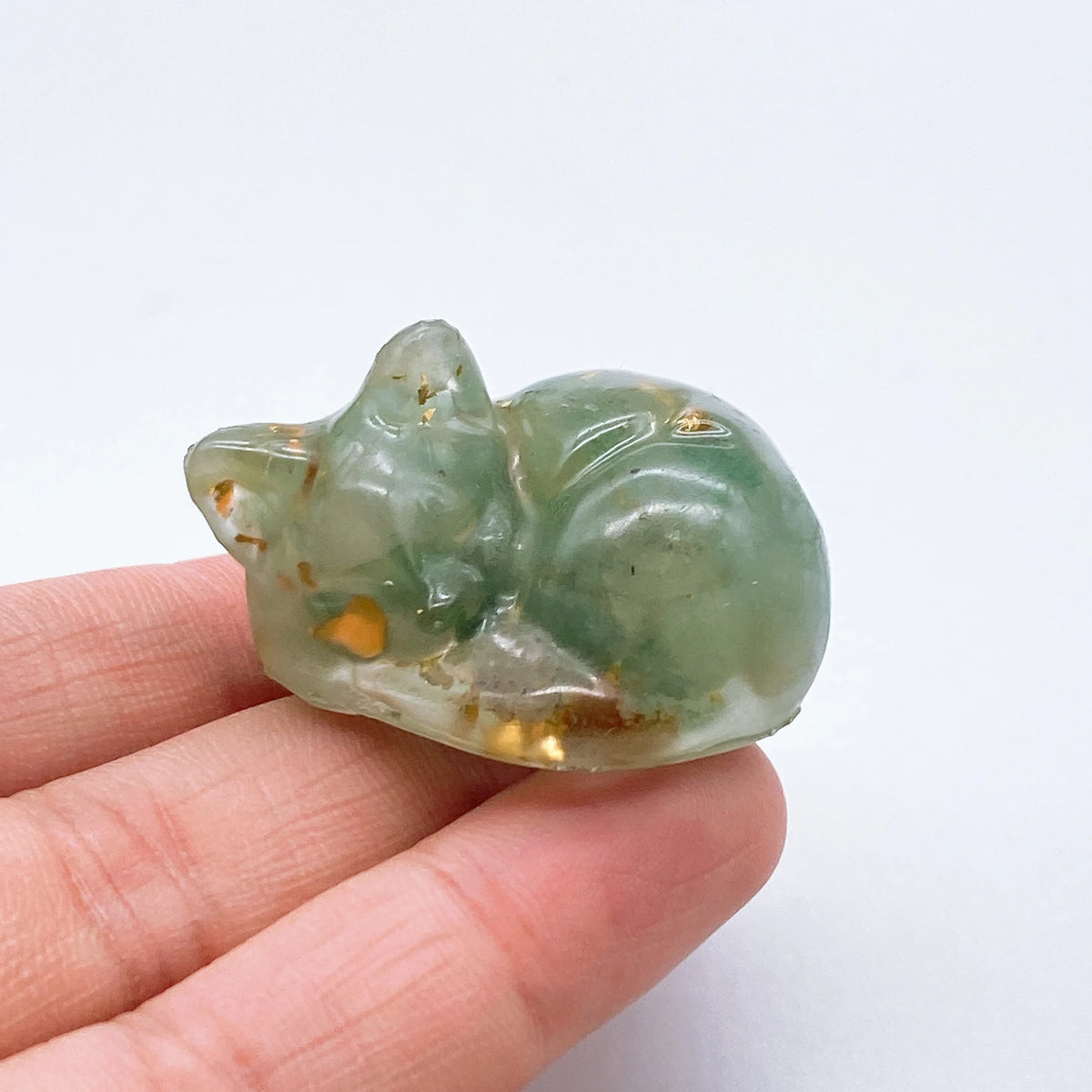 A smooth, translucent green crystal resin figurine shaped like a sleeping cat, held in a hand.