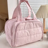 A soft pink quilted travel makeup bag with a wide opening is shown on a white surface.